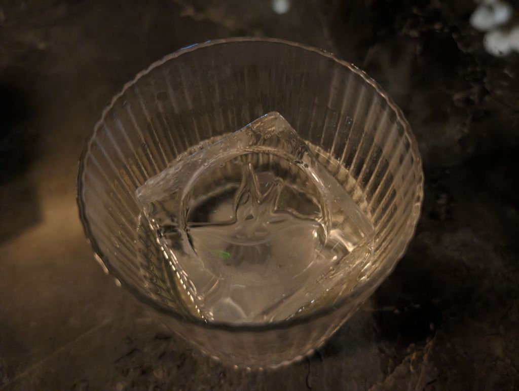 glass containing cocktail and large ice cube with hummingbird logo